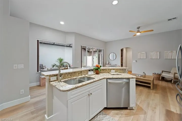 Kitchen featuring arched walkways, dishwasher, light wood-style flooring, white cabinetry, and a sink