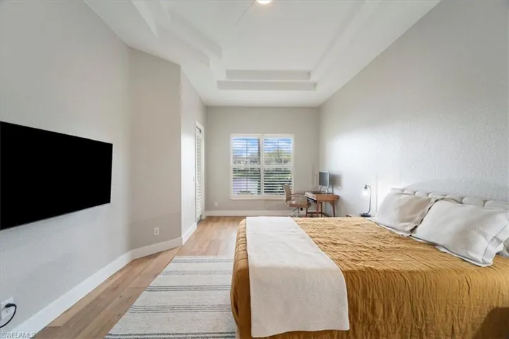 Bedroom featuring light wood-style flooring, a tray ceiling, and baseboards