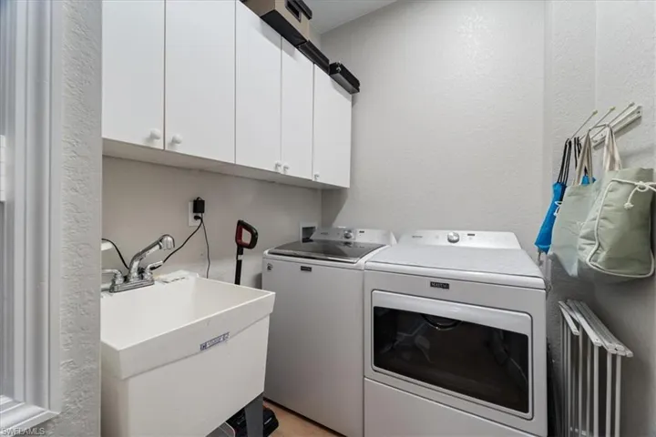 Laundry room featuring a textured wall, cabinet space, a sink, and washing machine and clothes dryer