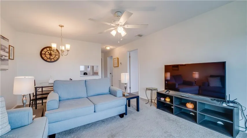 Open-concept living space featuring neutral wall paint, carpet flooring, a ceiling fan with integrated lighting, and an overhead chandelier in the dining area