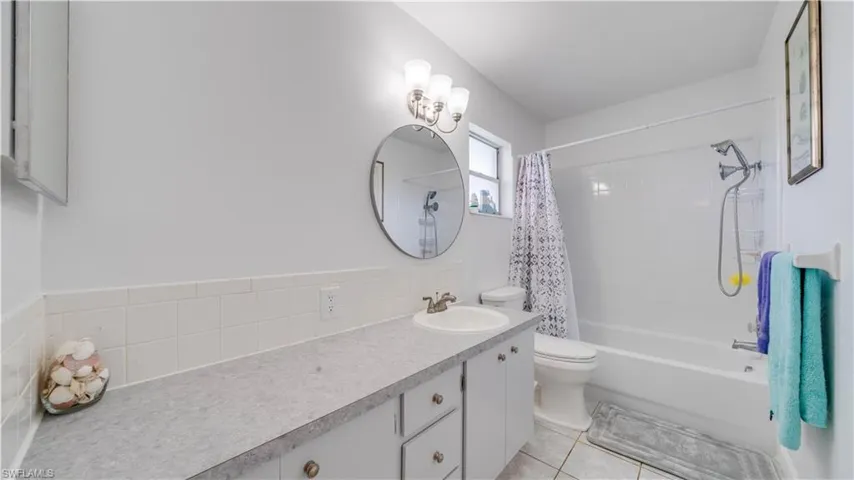 Bathroom featuring a single vanity with extensive countertop space, white cabinetry, a circular mirror, and a full bathtub with shower