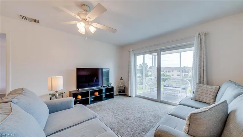 Carpeted living area with a ceiling fan, white walls, and sliding glass doors opening to a screened balcony