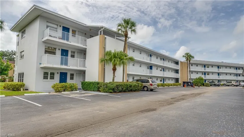 Multi-story building featuring balconies with white railings, exterior walkways, and mature palm trees