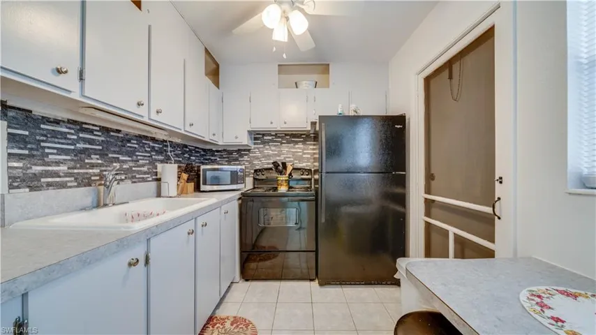 White cabinetry with brushed nickel hardware, mosaic tile backsplash, black appliance suite, and white tile flooring