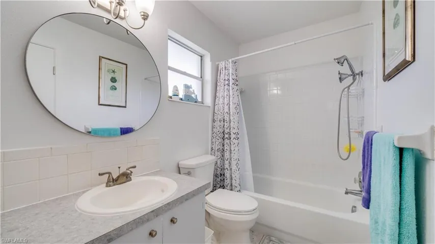 Vanity with an integrated sink, a large circular mirror, and a full bathtub with a shower