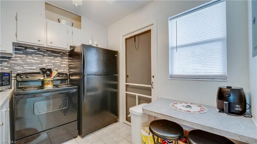 Kitchen featuring a black appliance package, white cabinetry, mosaic tile backsplash, and a breakfast bar