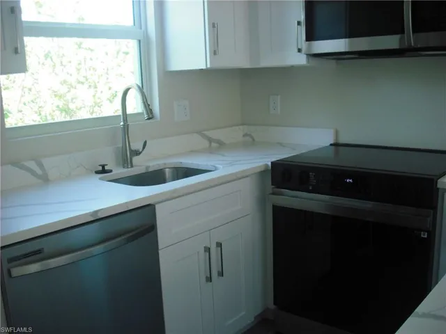 Kitchen featuring black electric range oven, white cabinetry, stainless steel microwave, a sink, and dishwashing machine
