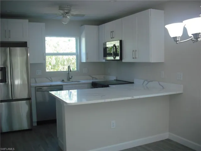 Kitchen with a sink, white cabinetry, appliances with stainless steel finishes, a peninsula, and dark wood-style floors