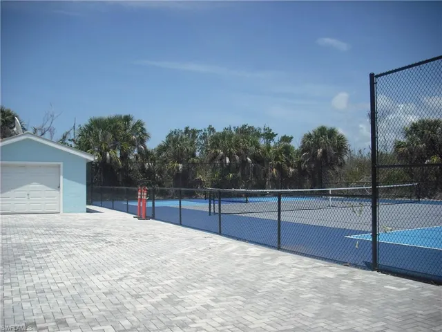 View of tennis court with fence and view of wooded area