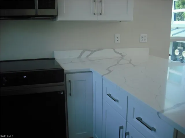 Kitchen featuring white cabinets, light stone countertops, and black electric range