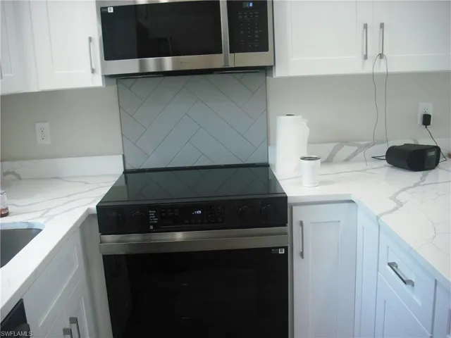 Kitchen featuring stainless steel microwave, range with electric stovetop, tasteful backsplash, white cabinetry, and light stone counters