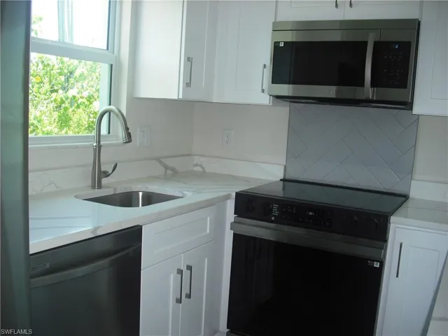 Kitchen with electric stove, stainless steel microwave, dishwashing machine, white cabinetry, and tasteful backsplash