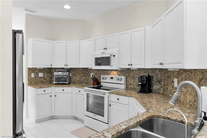 Kitchen featuring white appliances, white cabinets, backsplash, and recessed lighting