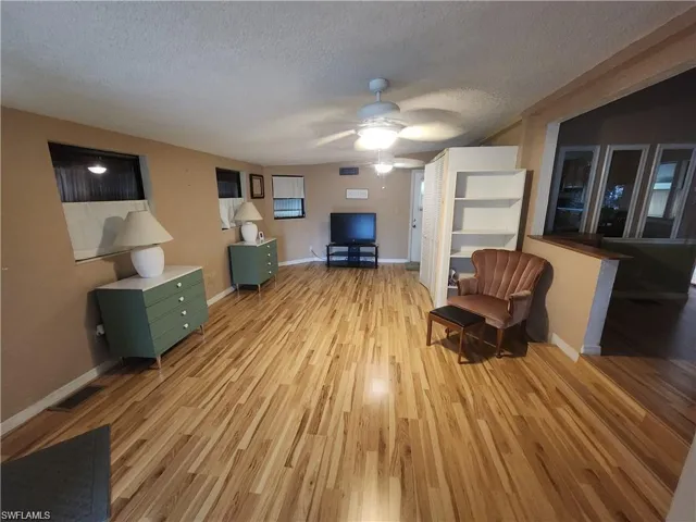 Living area featuring light wood-style flooring, a textured ceiling, and ceiling fan