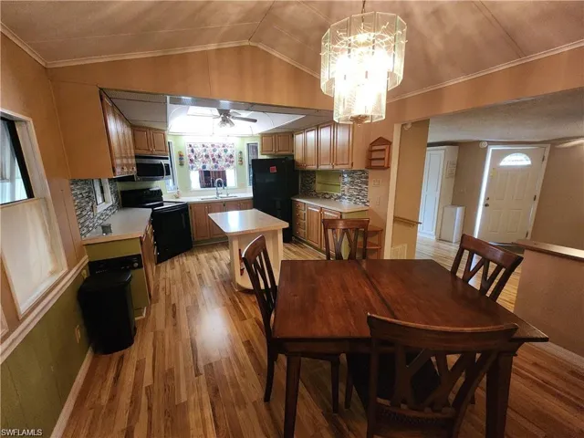 Dining room with lofted ceiling, crown molding, light wood-style floors, a ceiling fan, and a chandelier