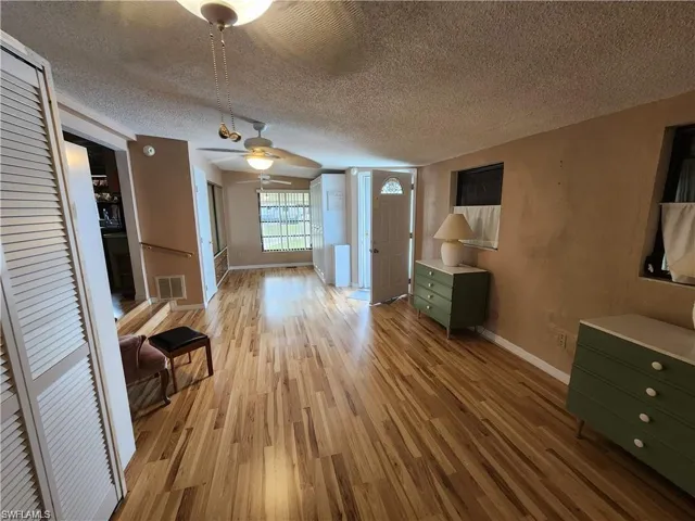 Unfurnished living room with light wood-style flooring, ceiling fan, and a textured ceiling