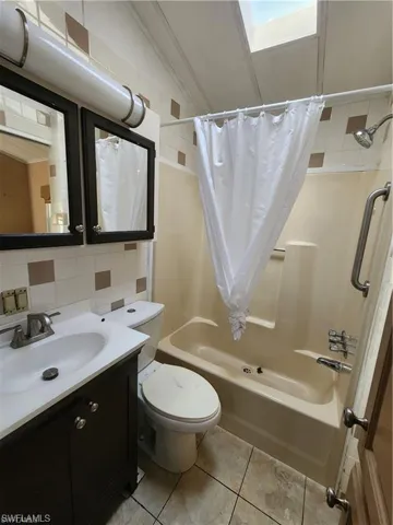 Bathroom featuring vanity, shower / tub combo with curtain, tile walls, and backsplash