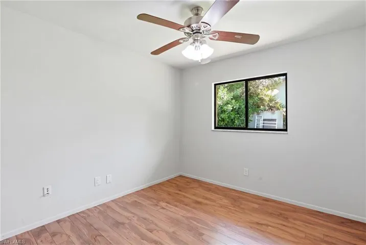 Room featuring wood-finish flooring, a ceiling fan with integrated lighting, and a window with black trim
