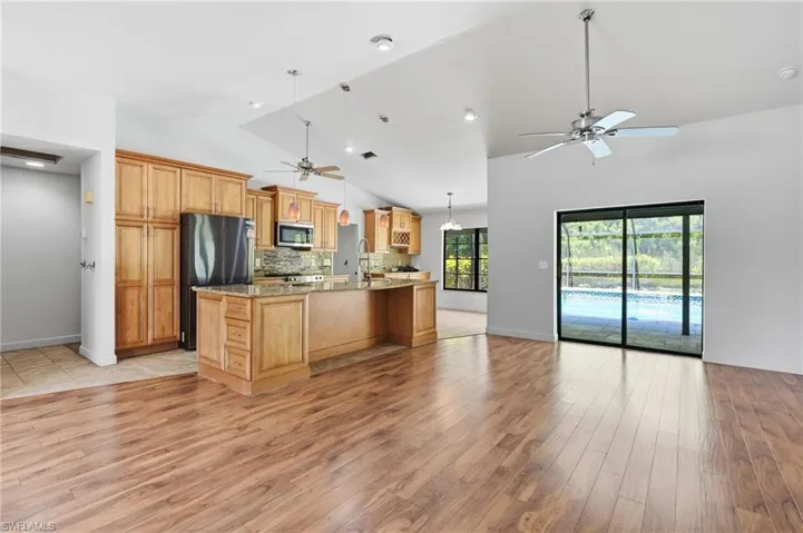 Vaulted ceilings define this open-concept space featuring wood-finish flooring, a kitchen island with stone countertops, and wood cabinetry