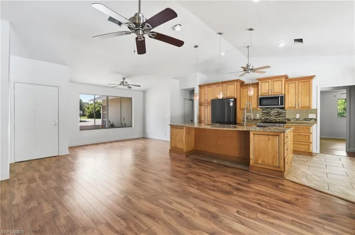 Open-concept living space featuring wood-finish flooring, vaulted ceilings, and multiple ceiling fans