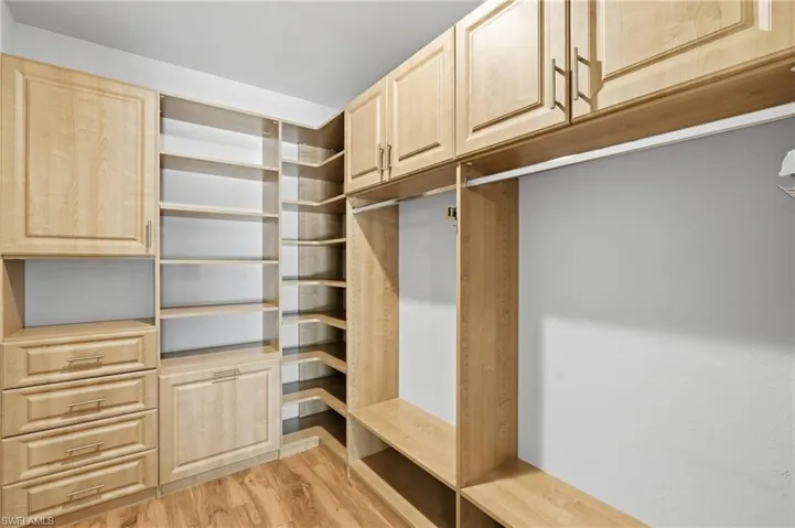 Custom closet organization system featuring wood-finish cabinetry, open shelving, integrated drawers, and hanging rods