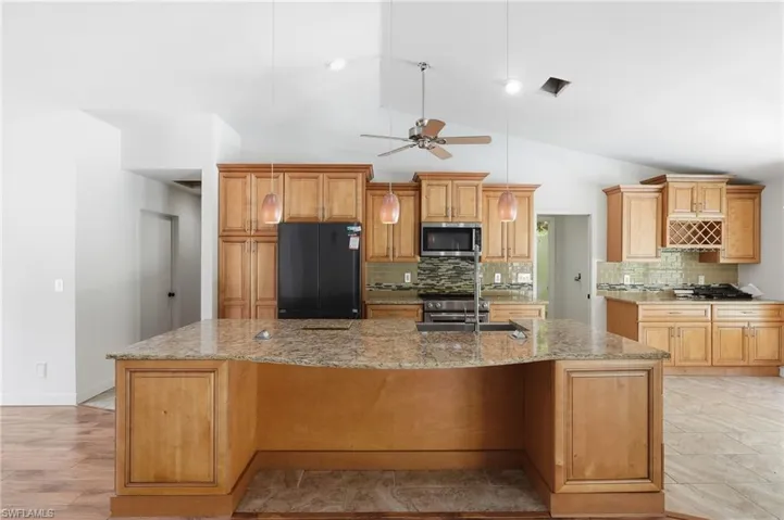 Spacious kitchen featuring an expansive center island with stone countertop, wood-finish cabinetry, tile backsplash, and a built-in wine rack