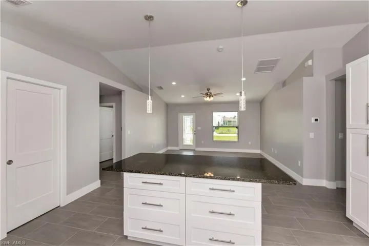Kitchen with white cabinets, dark stone counters, open floor plan, ceiling fan, and hanging light fixtures
