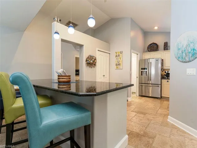 Kitchen featuring decorative light fixtures, stainless steel fridge with ice dispenser, a kitchen bar, dark stone countertops, and light tile floors