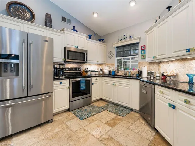 Kitchen featuring vaulted ceiling, tasteful backsplash, white cabinetry, and appliances with stainless steel finishes
