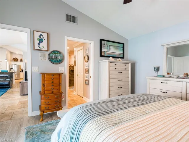 Bedroom featuring light tile flooring, vaulted ceiling, stainless steel refrigerator with ice dispenser, and ensuite bath