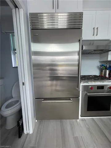 Kitchen with appliances with stainless steel finishes, under cabinet range hood, white cabinetry, and wood finish floors