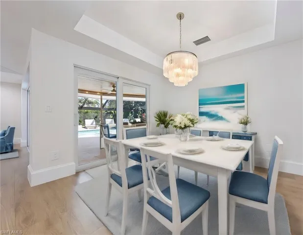 Dining room featuring an inviting chandelier, light hardwood / wood-style floors, and a tray ceiling