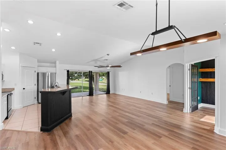 Kitchen featuring white cabinetry, ceiling fan, light wood-type flooring, stove, and a center island with sink