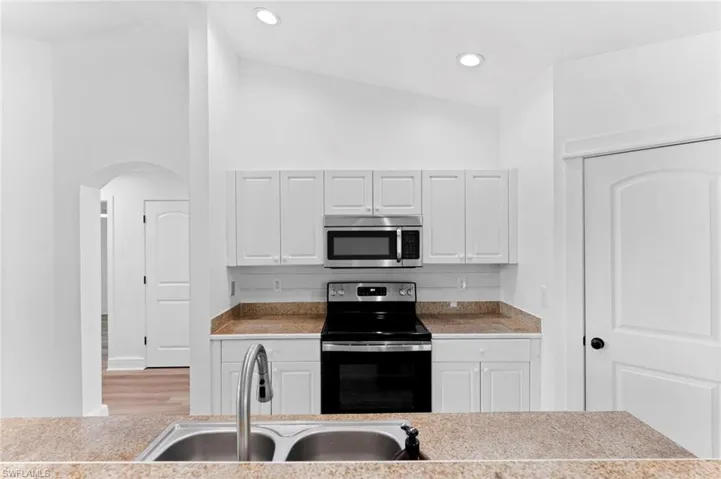 Kitchen with white cabinetry, lofted ceiling, stainless steel appliances, hardwood / wood-style floors, and sink