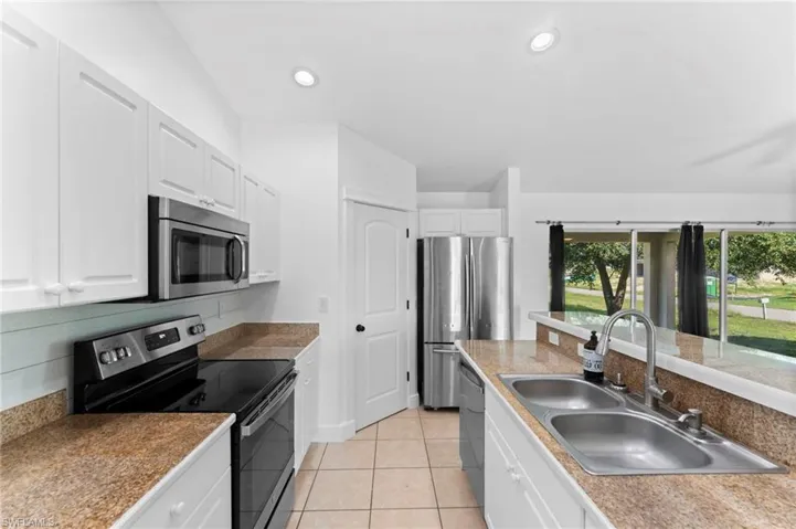 Kitchen with light tile patterned floors, white cabinetry, appliances with stainless steel finishes, and sink