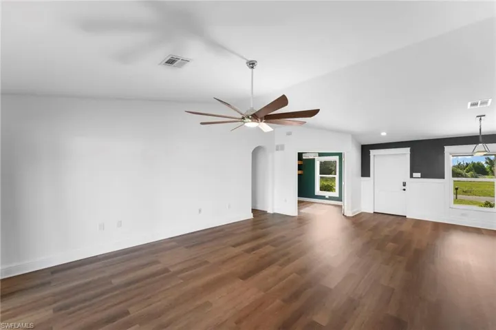 Unfurnished living room with dark wood-type flooring, ceiling fan, lofted ceiling, and a wealth of natural light