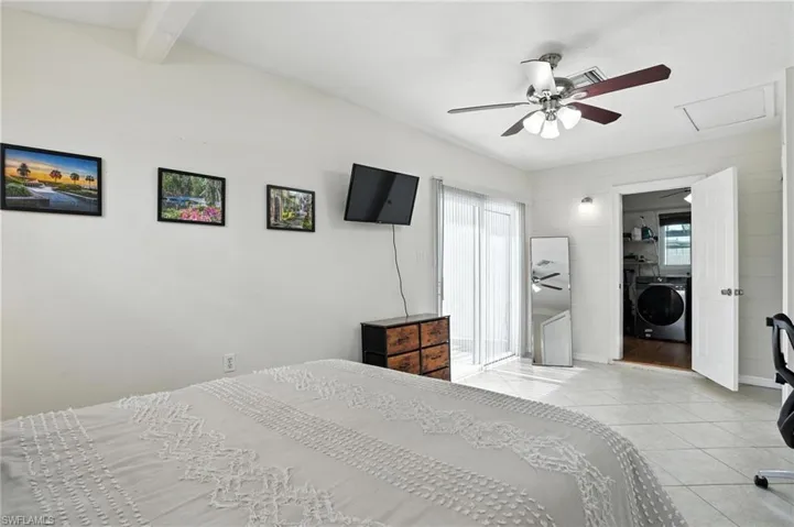 Tiled bedroom featuring washer / clothes dryer, multiple windows, beamed ceiling, attic access, and a ceiling fan