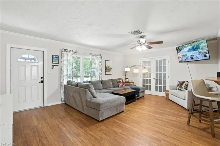 Living area featuring french doors, light wood-type flooring, a ceiling fan, ornamental molding, and a textured ceiling