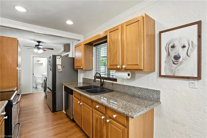 Kitchen featuring stainless steel appliances, crown molding, a textured wall, a ceiling fan, and light wood-style floors