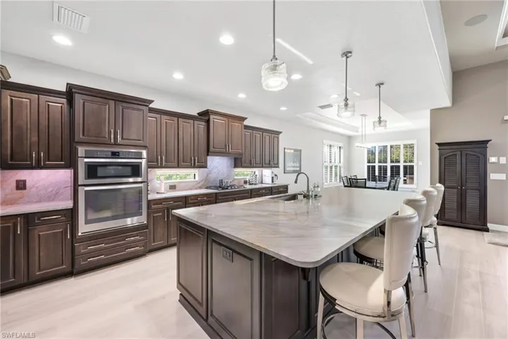 Kitchen featuring dark brown cabinetry, a raised ceiling, a center island with sink, pendant lighting, and recessed lighting