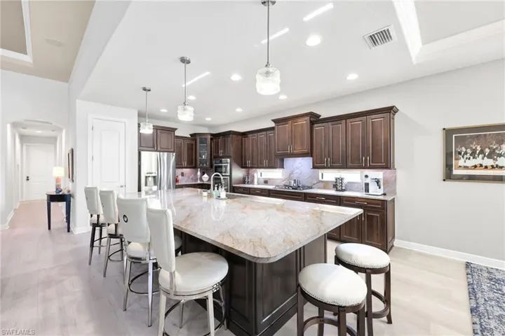 Kitchen with dark brown cabinetry, a kitchen breakfast bar, hanging light fixtures, arched walkways, and recessed lighting