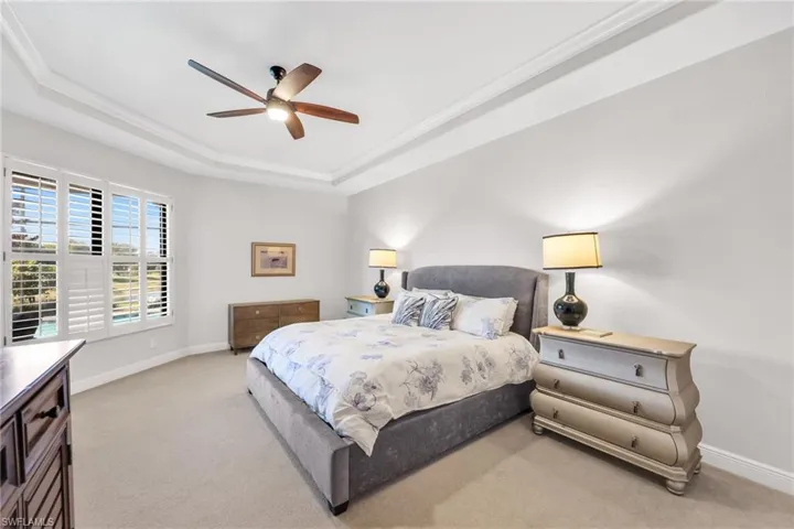 Bedroom featuring a raised ceiling, a ceiling fan, light colored carpet, and crown molding