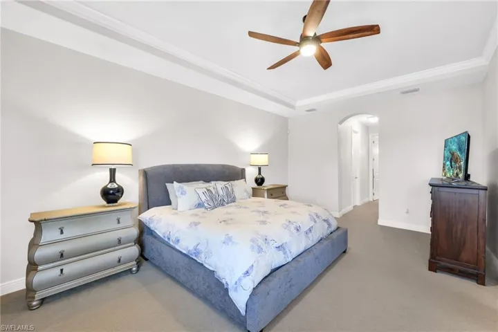 Carpeted bedroom featuring a ceiling fan, arched walkways, and a raised ceiling