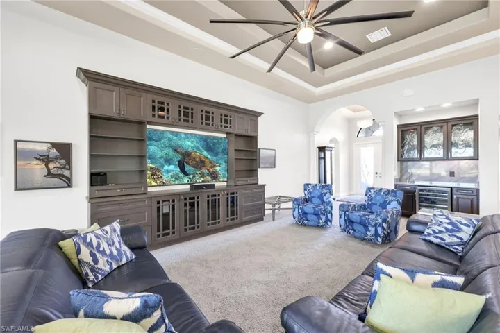 Carpeted living area with arched walkways, a bar, wine cooler, a raised ceiling, and recessed lighting