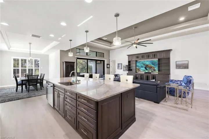 Kitchen featuring dark brown cabinets, light stone countertops, light wood-type flooring, hanging light fixtures, and a kitchen island with sink