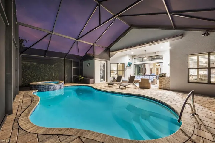 View of pool featuring glass enclosure, a patio area, a pool with connected hot tub, and an outdoor living space