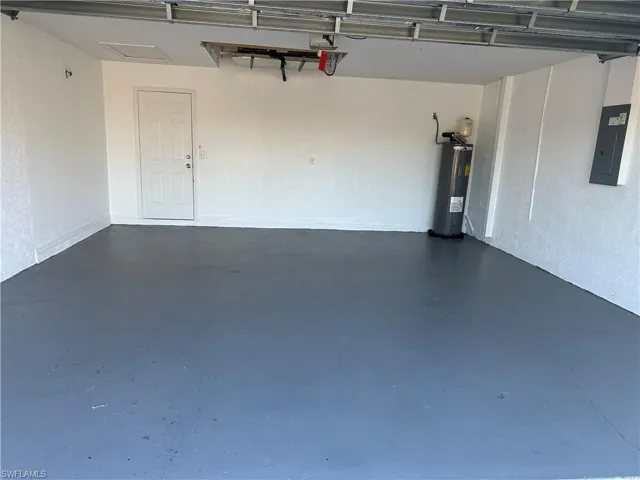 Garage featuring electric water heater, electric panel, and a garage door opener