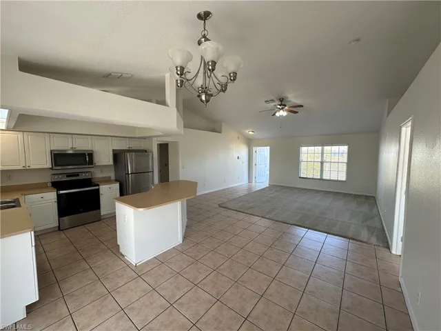 Kitchen with light tile patterned floors, ceiling fan with notable chandelier, vaulted ceiling, and appliances with stainless steel finishes