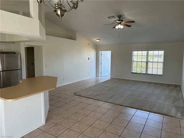 Kitchen featuring ceiling fan with notable chandelier, stainless steel fridge, light tile patterned flooring, and high vaulted ceiling