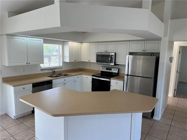 Kitchen with white cabinets, appliances with stainless steel finishes, light tile patterned floors, and sink